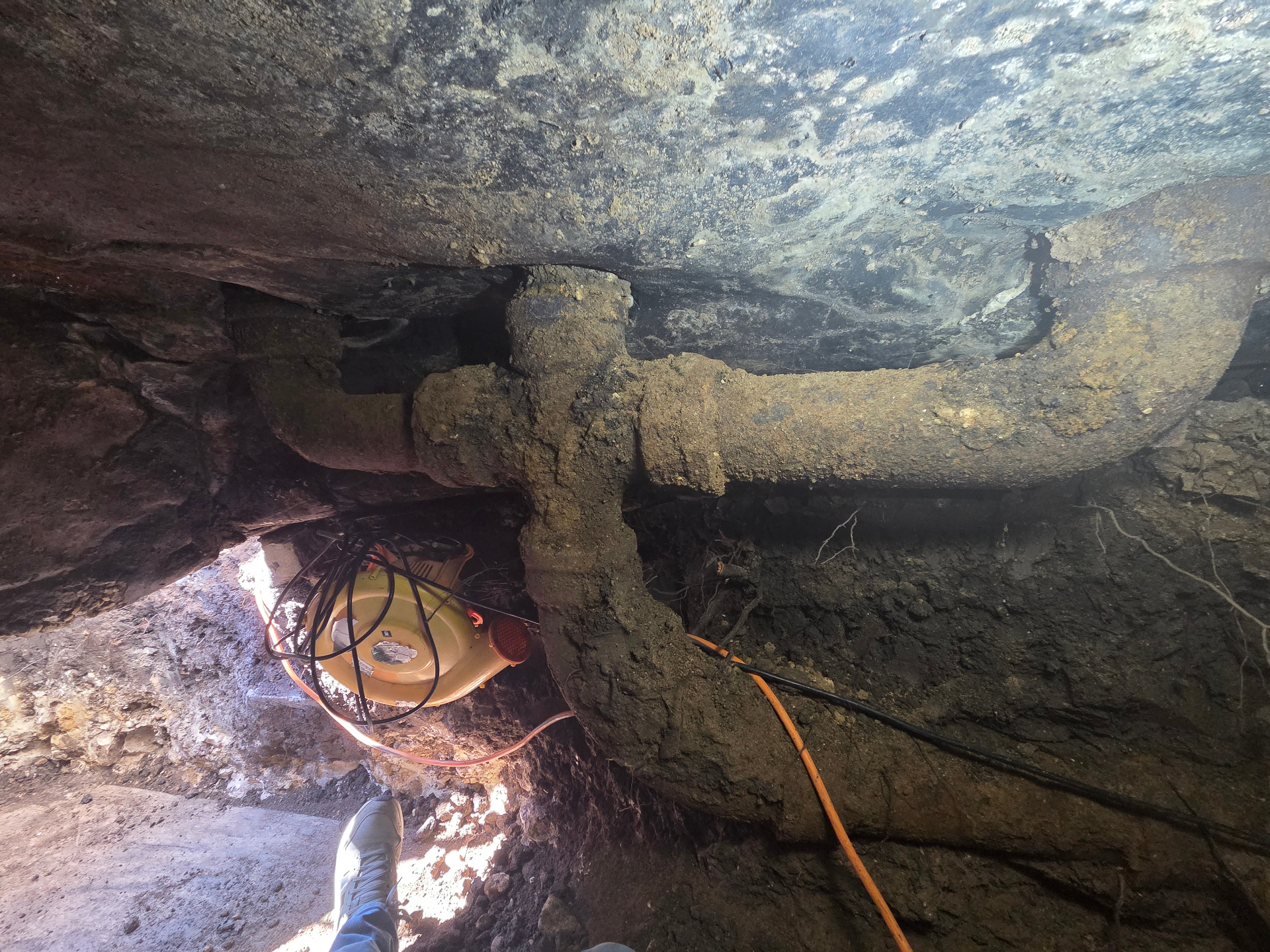 Tubería de hierro fundido expuesta dentro de túnel bajo losa con equipo de ventilación
